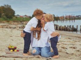 Am Stand in Dänemark, zwei Kinder umarmen und küssen ihre Mutter, genießen dabei die milde Sonne