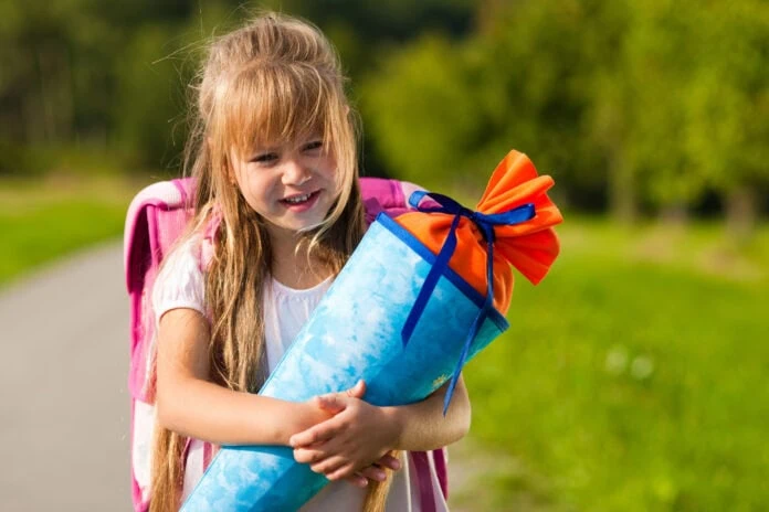 Lächelndes Mädchen mit blauer Schultüte bereit für die Einschulung mit 6 oder 7 Jahren - der Stichtag ist entscheidend