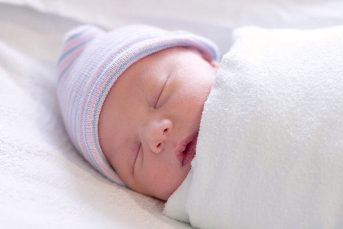 Friedlich schlafendes Neugeborenes in weißer Puckdecke mit gestreifter Mütze - Baby pucken nachts sorgt für Geborgenheit
