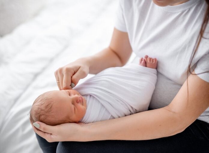 Neugeborenes Baby in weißes Tuch gepuckt wird von einer Person gehalten - Informationen, wann Baby Pucken gefährlich sein kann