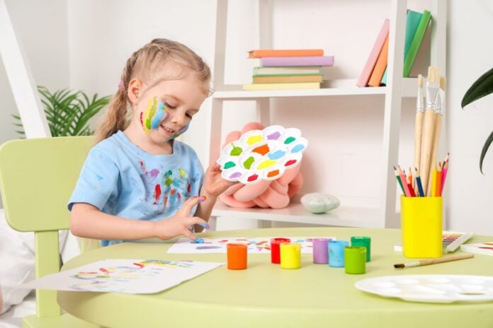 Fröhliches Kind mit Farbflecken malt kreativ mit bunten Farben für Klorollen-Tiere Bastelprojekt